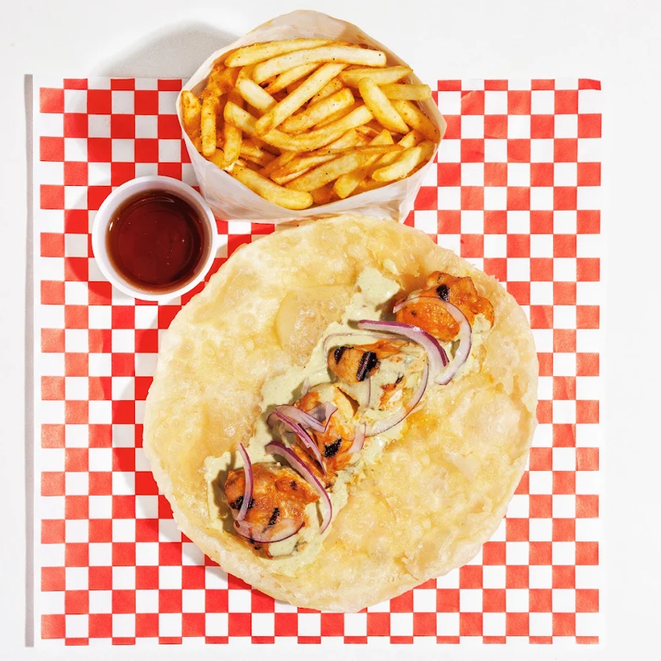 Flatbread wrap with grilled chicken, red onions, creamy sauce, fries, and dipping sauce on red-and-white checkered paper.